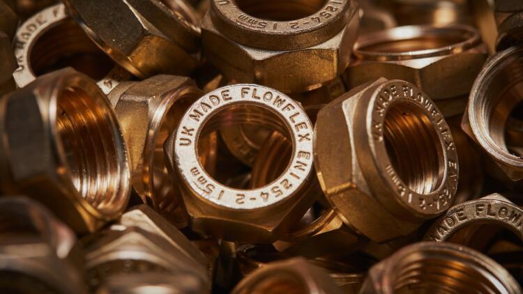 A close-up image of multiple brass nuts, each stamped with the Flowflex brand