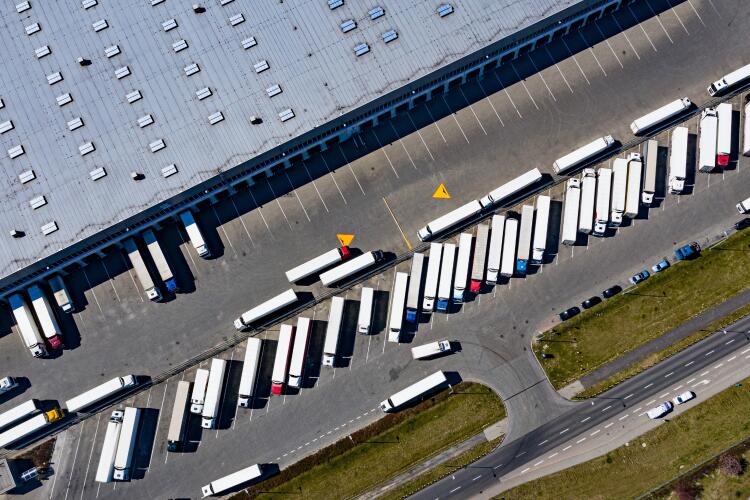 An aerial view of a large distribution centre with numerous white lorries parked in loading bays and lined up in the parking area. The image showcases the logistical operations and distribution capabilities of Flowflex products.