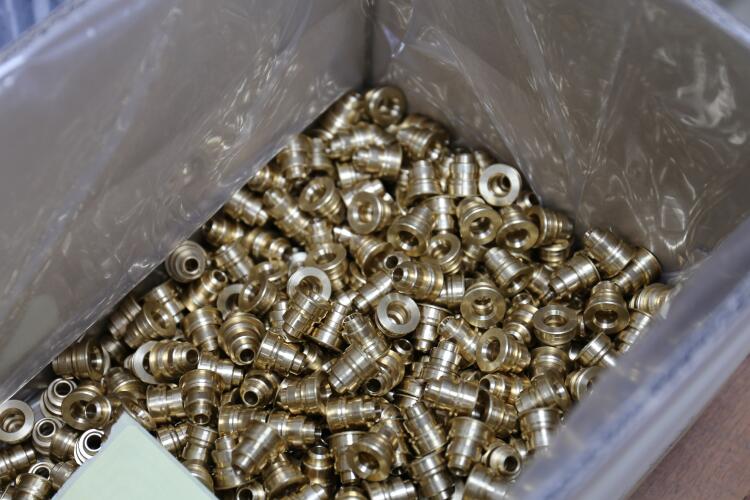 A bin filled with brass fittings, showcasing the variety and volume of precision components manufactured by Flowflex for diverse plumbing and HVAC needs.