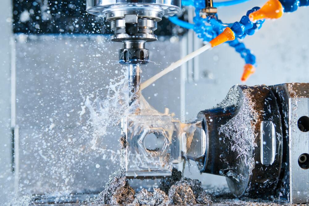 A close-up view of a CNC machine in operation, with a metal piece being precisely drilled and milled. Coolant fluid is sprayed onto the workpiece, creating splashes and metal shavings. The scene captures the modern manufacturing capabilities at Flowflex.