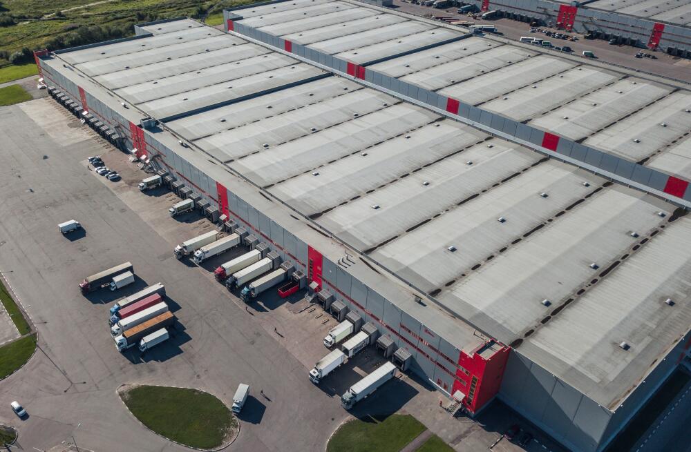 An aerial view of a large warehouse facility with multiple loading bays, where several lorries are parked and being loaded or unloaded. Indicating the logistics capabilities of Flowflex.